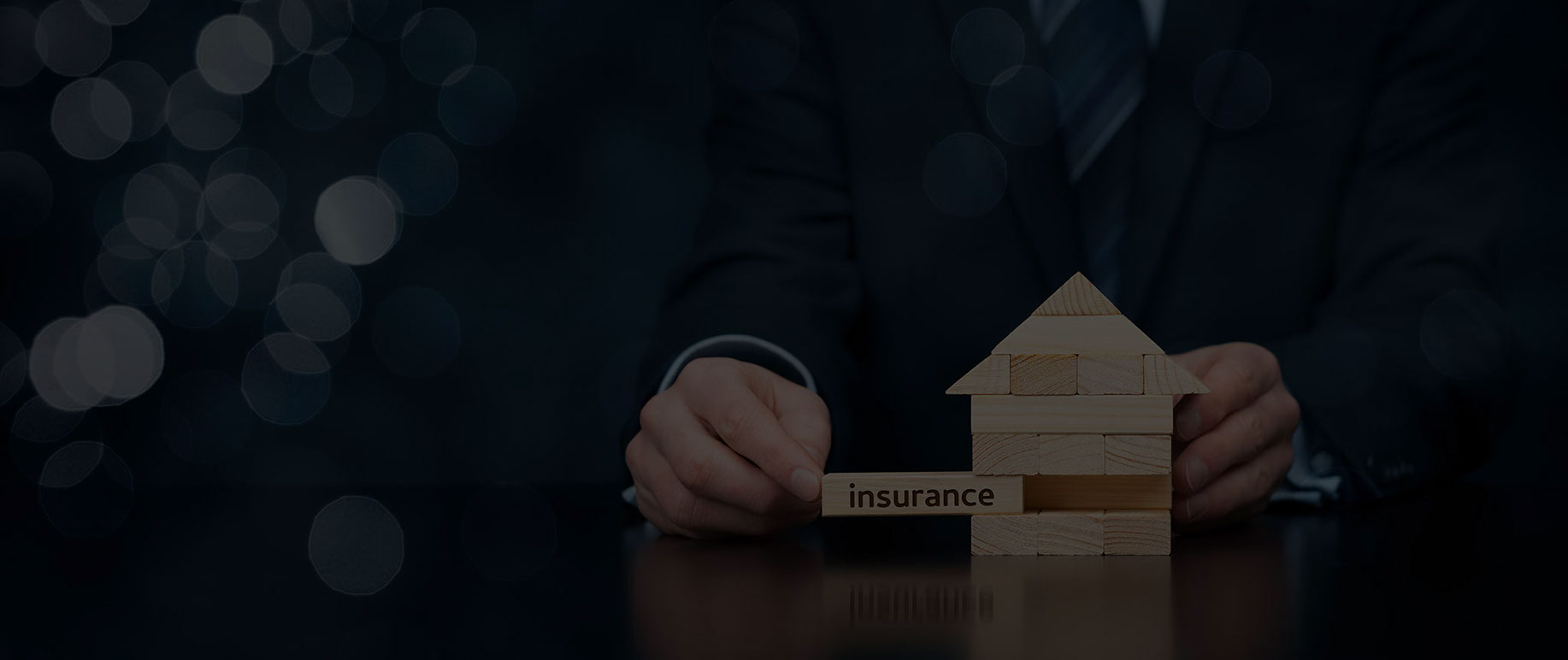 A wooden block labelled insurance being pushed into a gap in a small house made of blocks